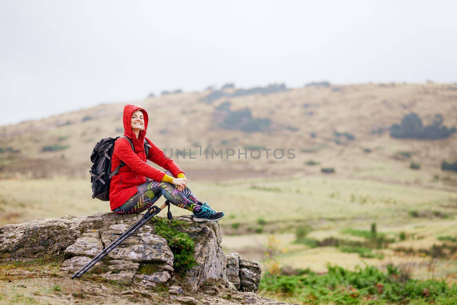 Hiker girl taking a rest on a rock in the mountains. Windy day. Travel and healthy lifestyle outdoors in fall season by kokimk