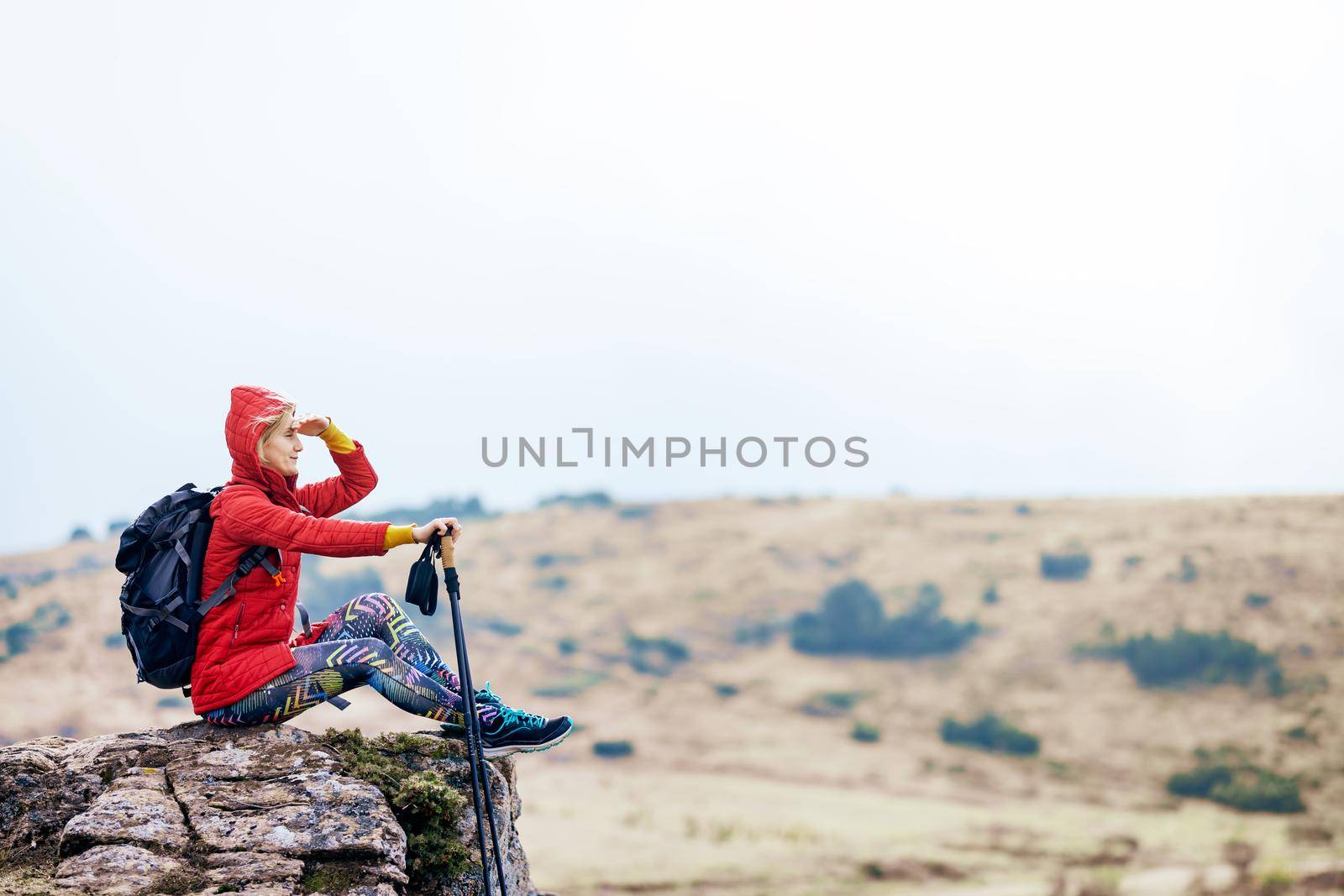 Hiker girl taking a rest on a rock in the mountains. Enjoying the view. Travel and healthy lifestyle outdoors in fall season