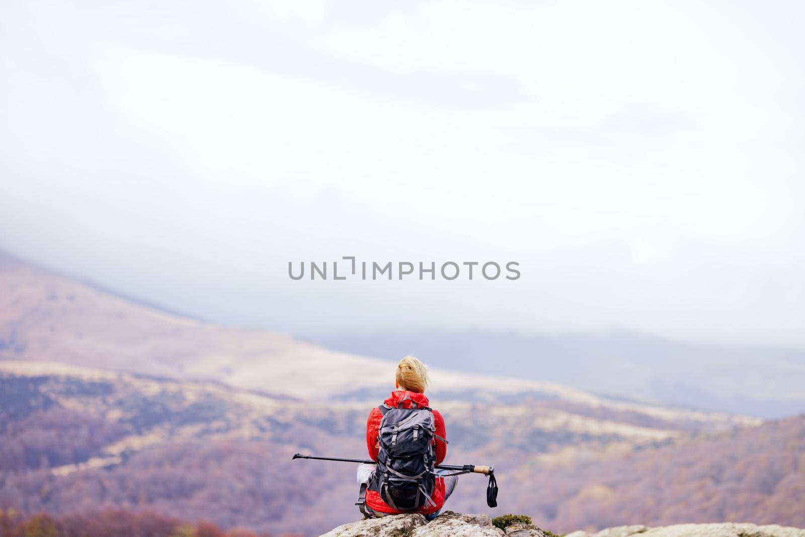 Hiker girl taking a rest on a rock in the mountains. Windy day. Travel and healthy lifestyle outdoors in fall season by kokimk