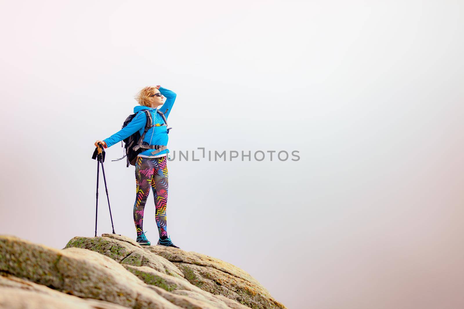 Hiking girl with poles and backpack standing on rocks. Windy autumn day. Travel and healthy lifestyle outdoors in fall season