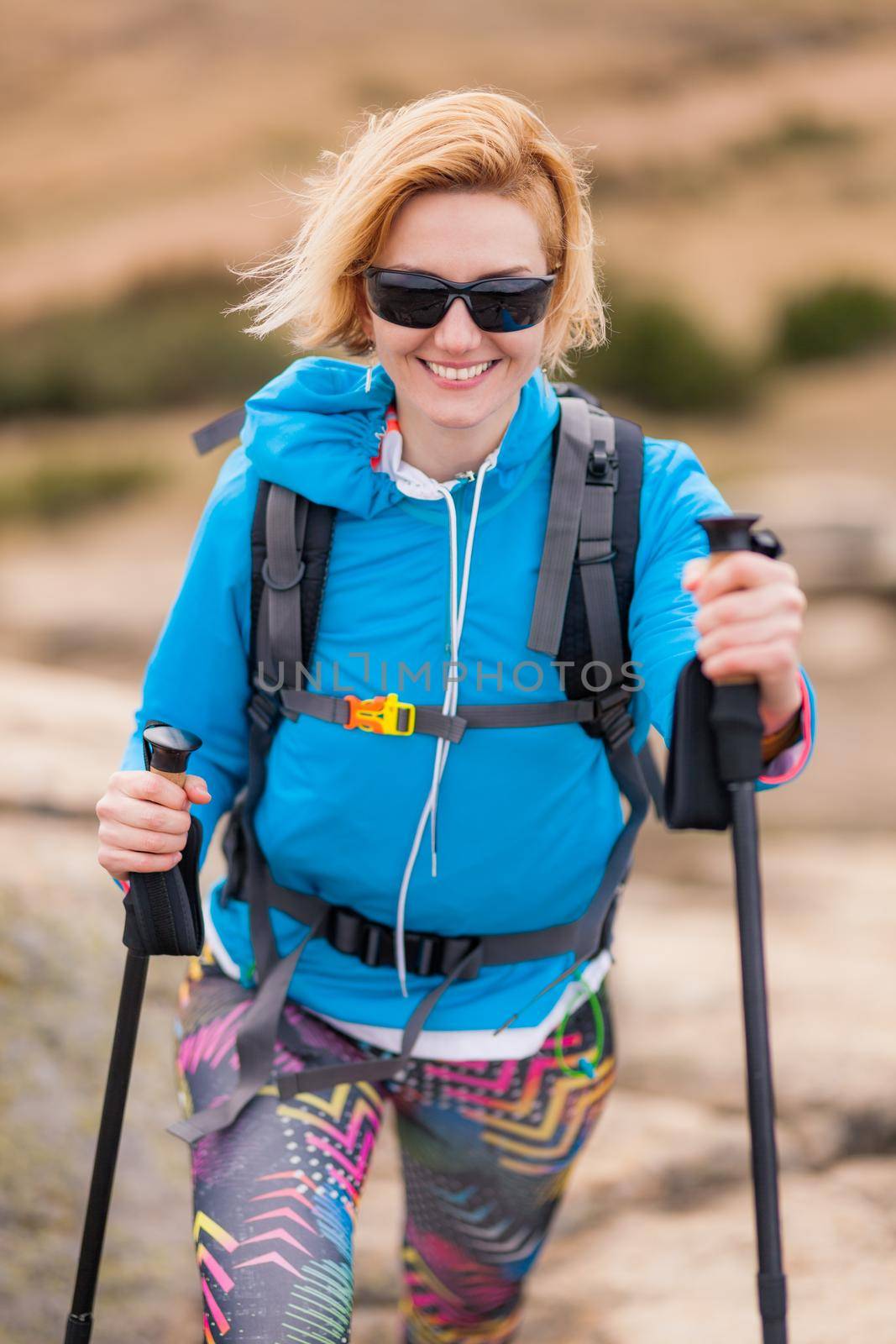 Hiking girl with poles and backpack standing on rocks. Windy autumn day. Travel and healthy lifestyle outdoors in fall season by kokimk