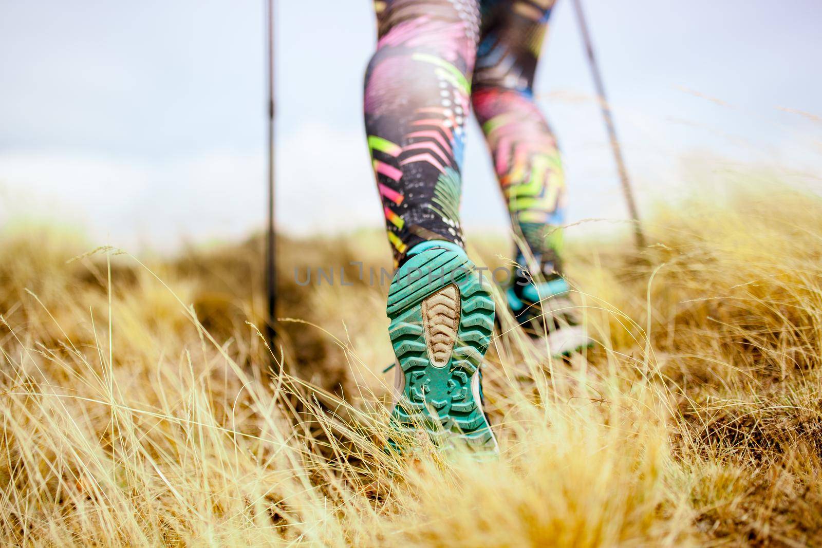 Hiking girl in a mountain meadow. Low angle view of generic sports shoe and legs on grass. Healthy fitness lifestyle outdoors.