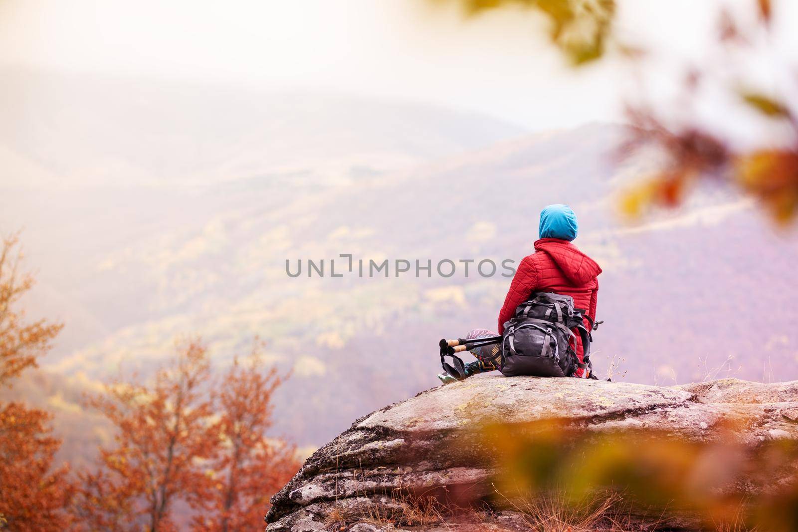 Hiker girl taking a rest on a rock in the mountains. Windy day. Travel and healthy lifestyle outdoors in fall season
