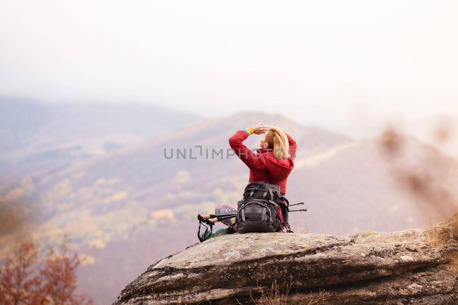 Hiker girl taking a rest on a rock in the mountains. Windy day. Travel and healthy lifestyle outdoors in fall season by kokimk