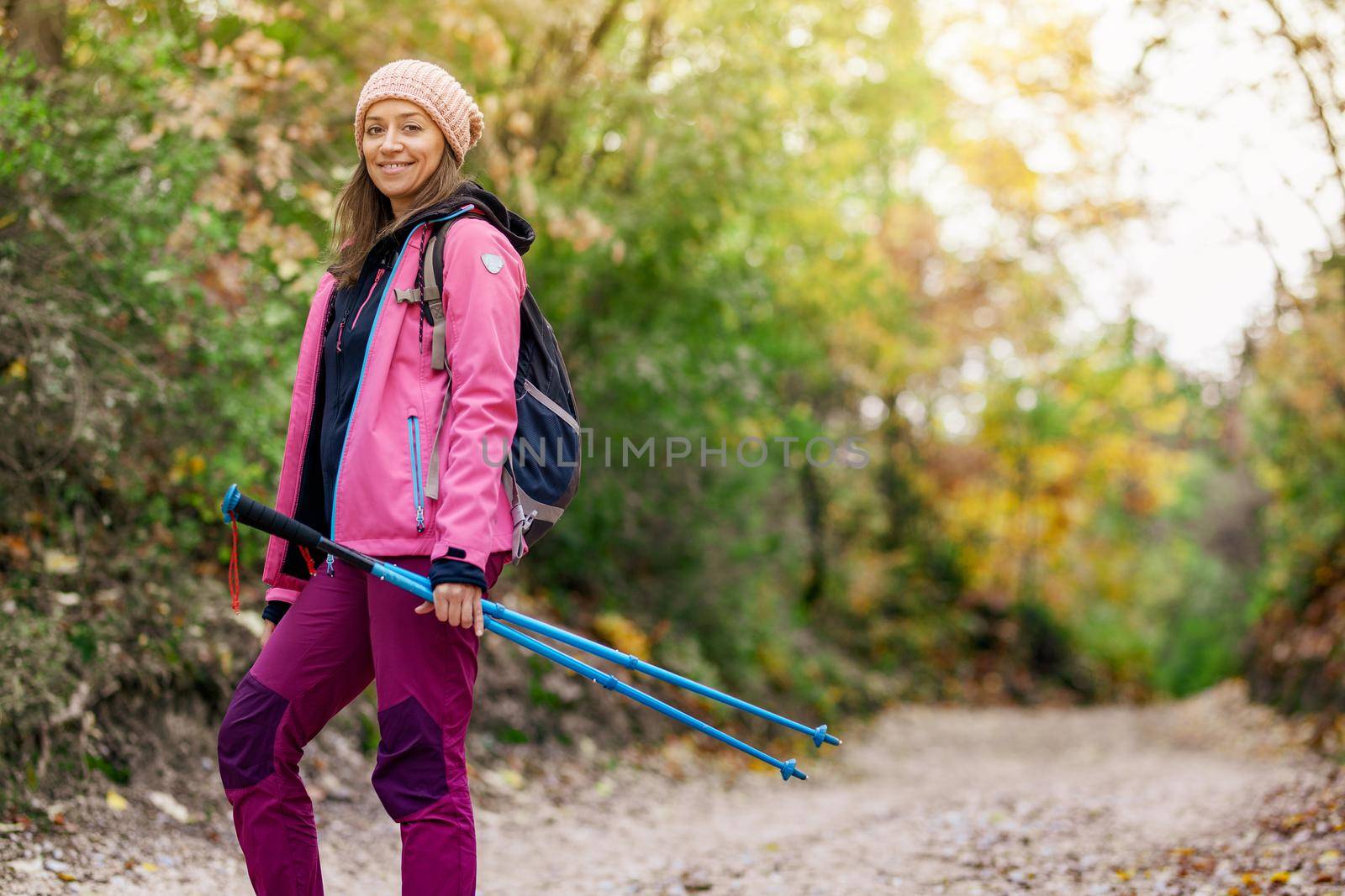 Hiker girl standing on a wide trail in the mountains. Backpacker with pink jacket in a forest. Healthy fitness lifestyle outdoors.