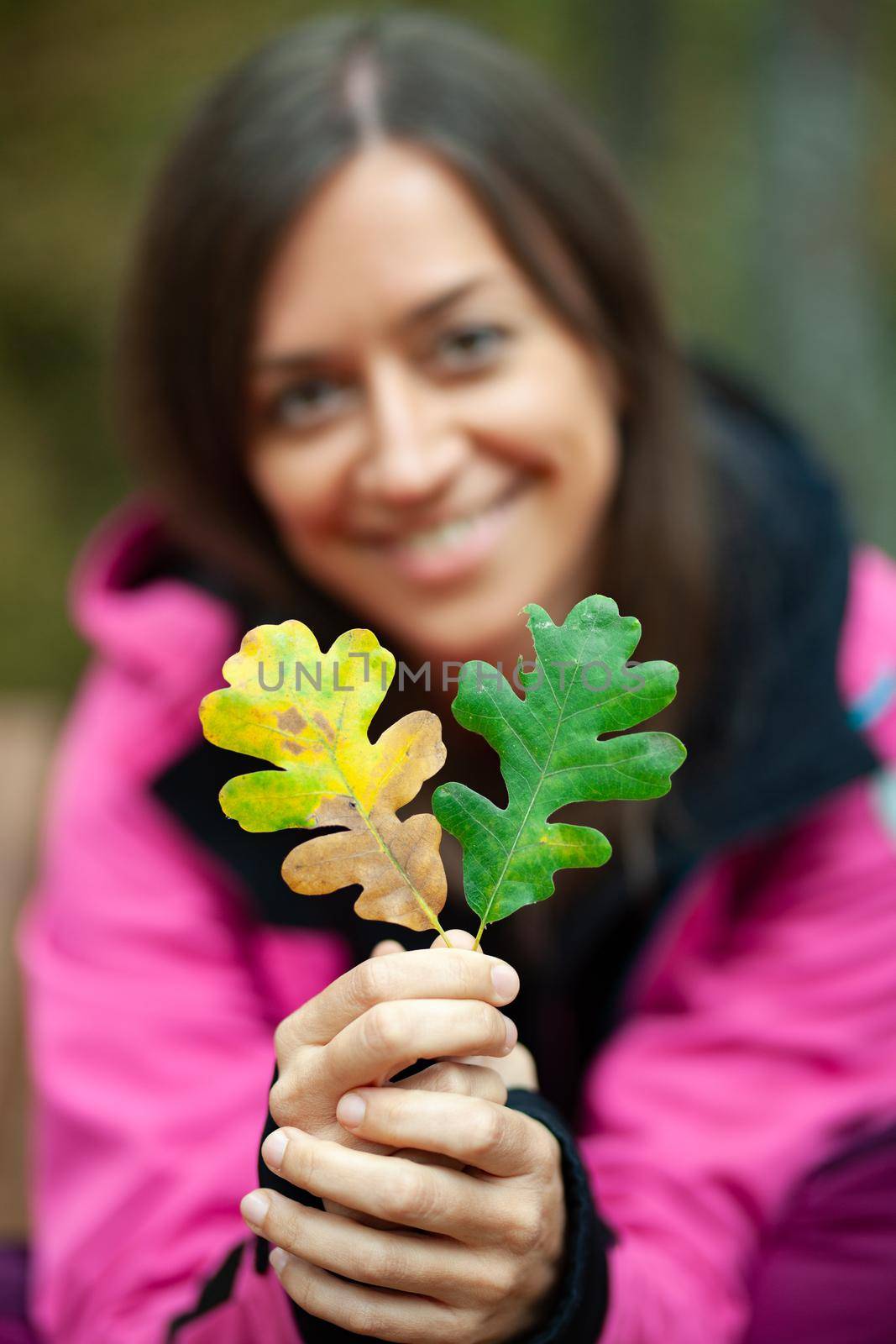 Girl in pink holding two autumn leaves. Fall season in the mountaing. Focus on leaves.