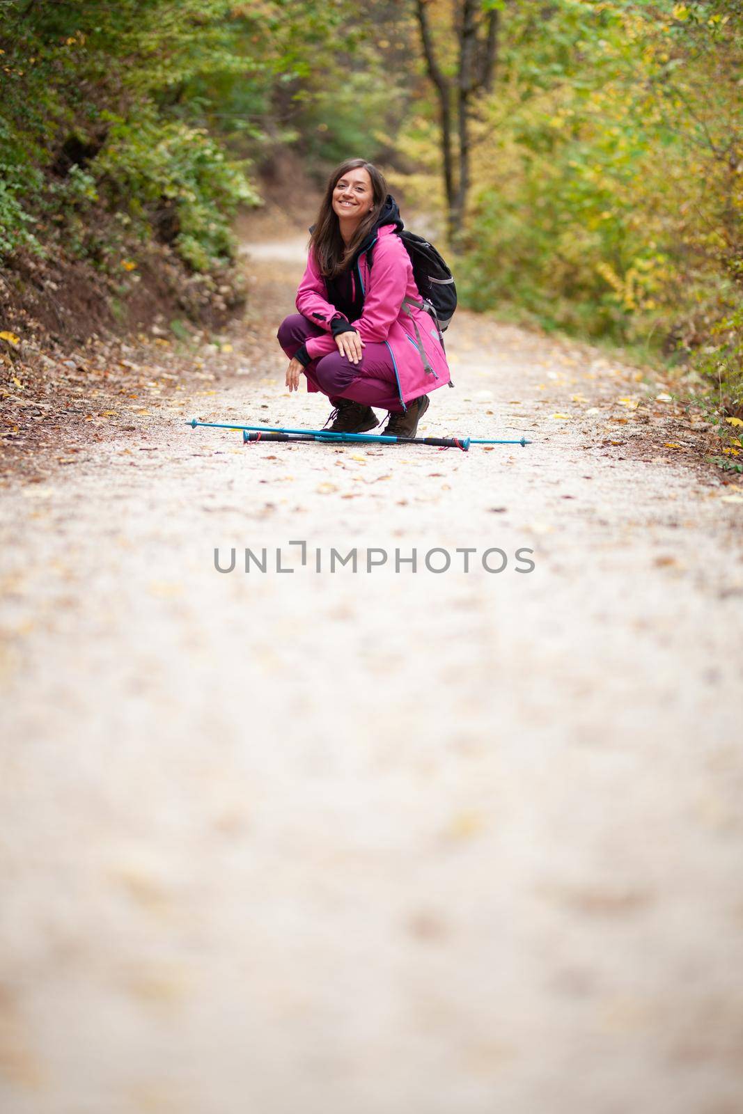 Hiker girl crouching on a trail in the mountains. Backpacker with pink jacket in a forest. Healthy fitness lifestyle outdoors.