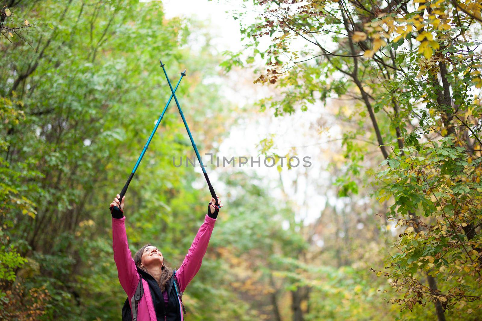 Hiking girl with poles and backpack on a trail. Hands up enjoying in nature. Travel and healthy lifestyle outdoors in fall season.