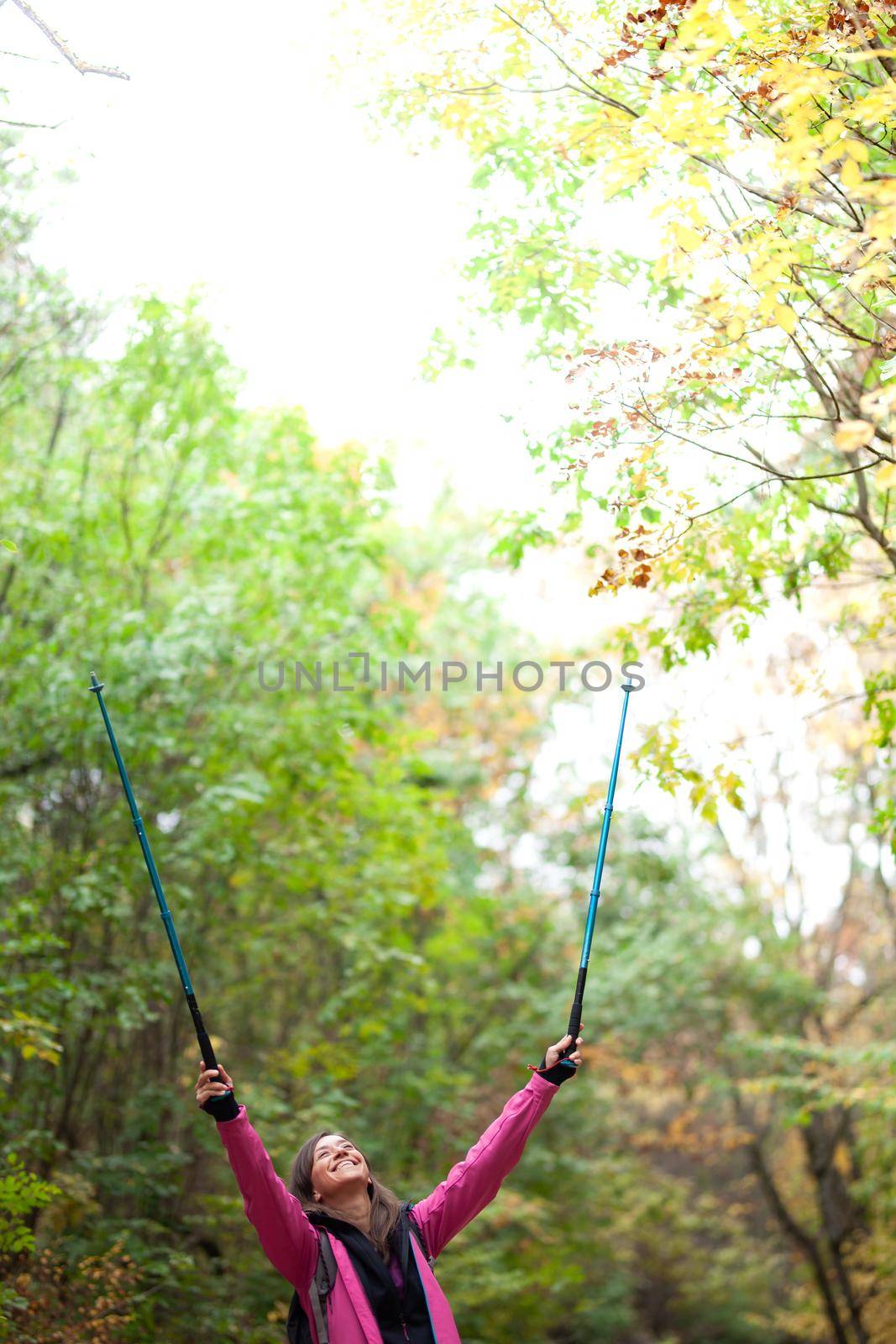 Hiking girl with poles and backpack on a trail. Hands up enjoying in nature. Travel and healthy lifestyle outdoors in fall season. by kokimk