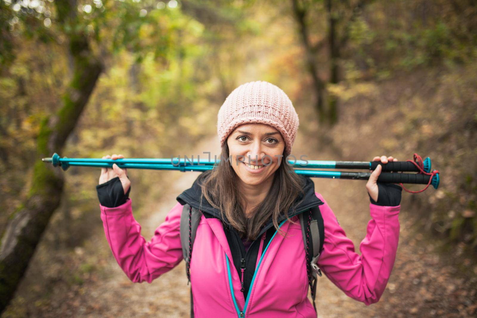 Hiker girl in pink on a trail in the forest. Looking at camera with poles in hands. Nature in fall season.