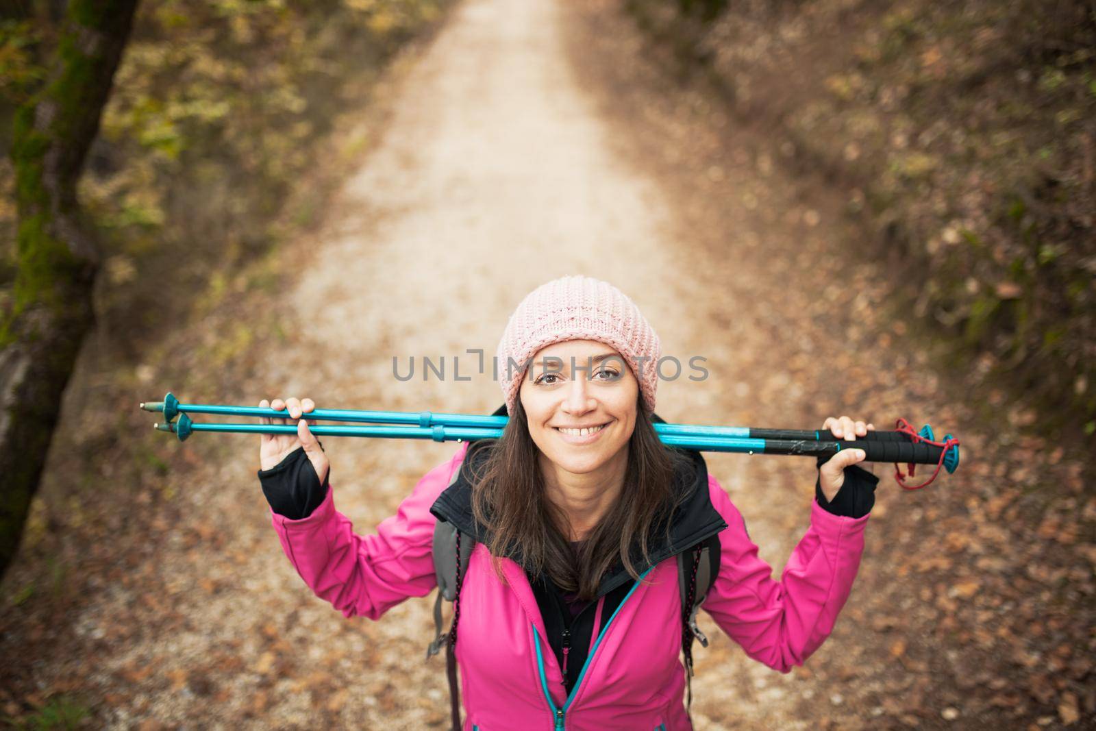 Hiker girl in pink on a trail in the forest. Looking at camera with poles in hands. Nature in fall season.