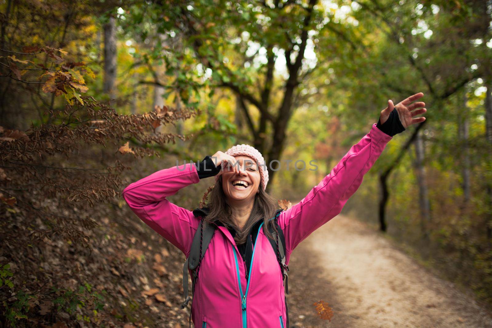 Hiking girl in pink on a trail in the forest. Hands up enjoying the falling leaves in nature in fall season.