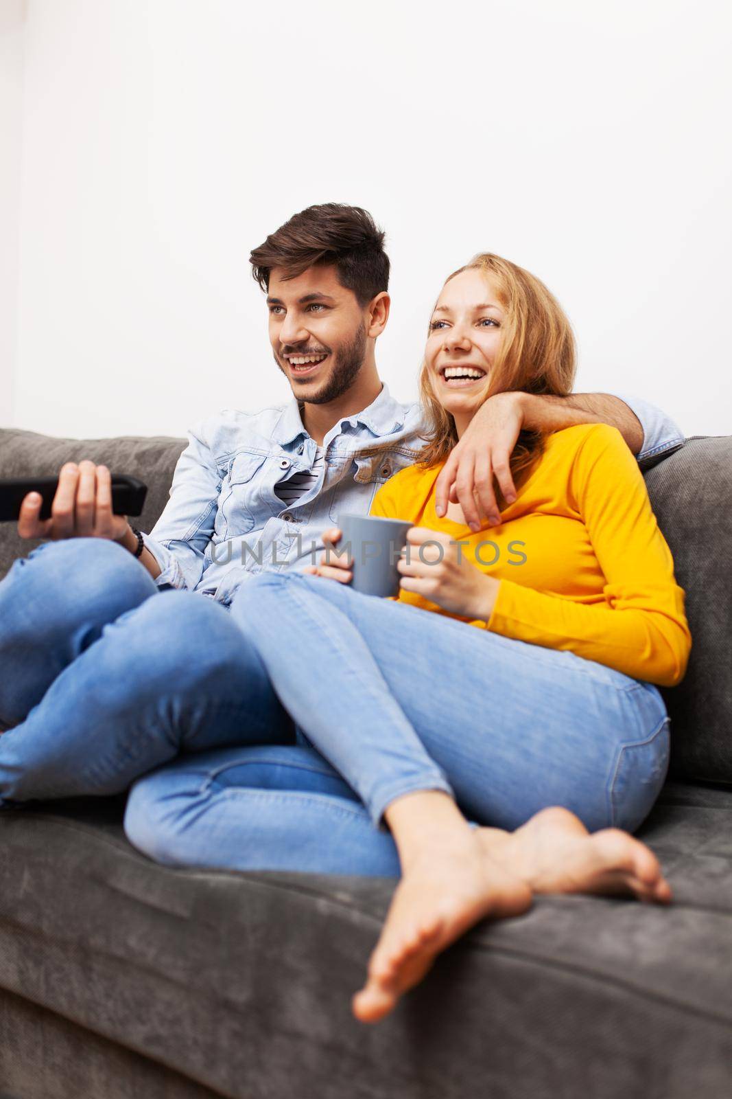 couple in love on a sofa at home, watching tv and smiling