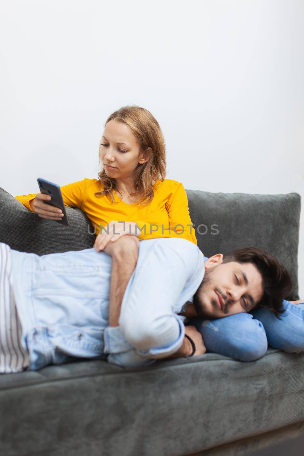 boy naps on girlfriend's lap while she looks at smart phone