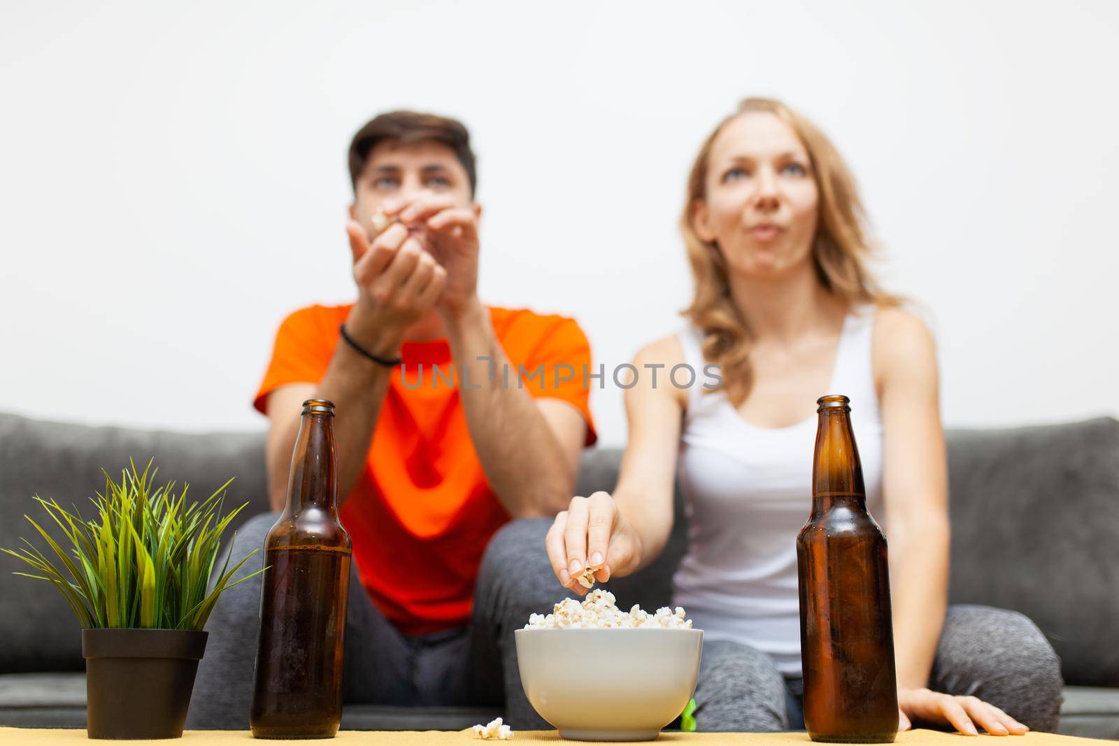 couple with beer bottles and popcorn watching sports game on tv. focus on bottles by kokimk