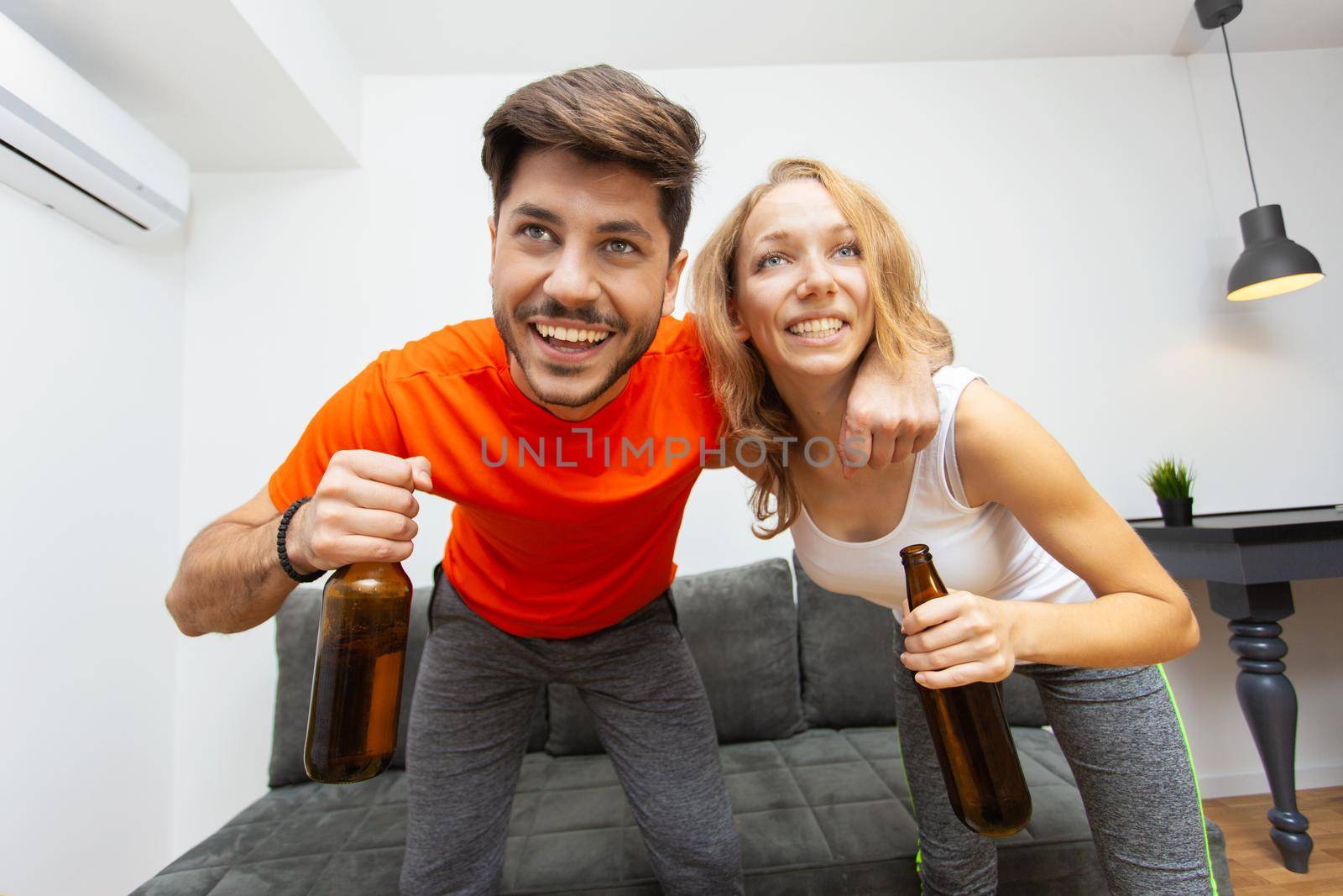 couple with beer bottles watching sports game on tv by kokimk