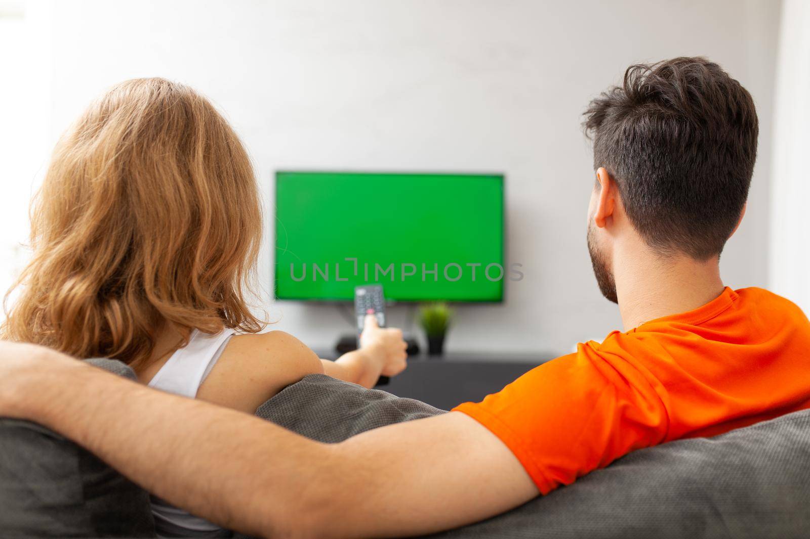 Couple watching tv with green screen. Girl pressing remote control. by kokimk