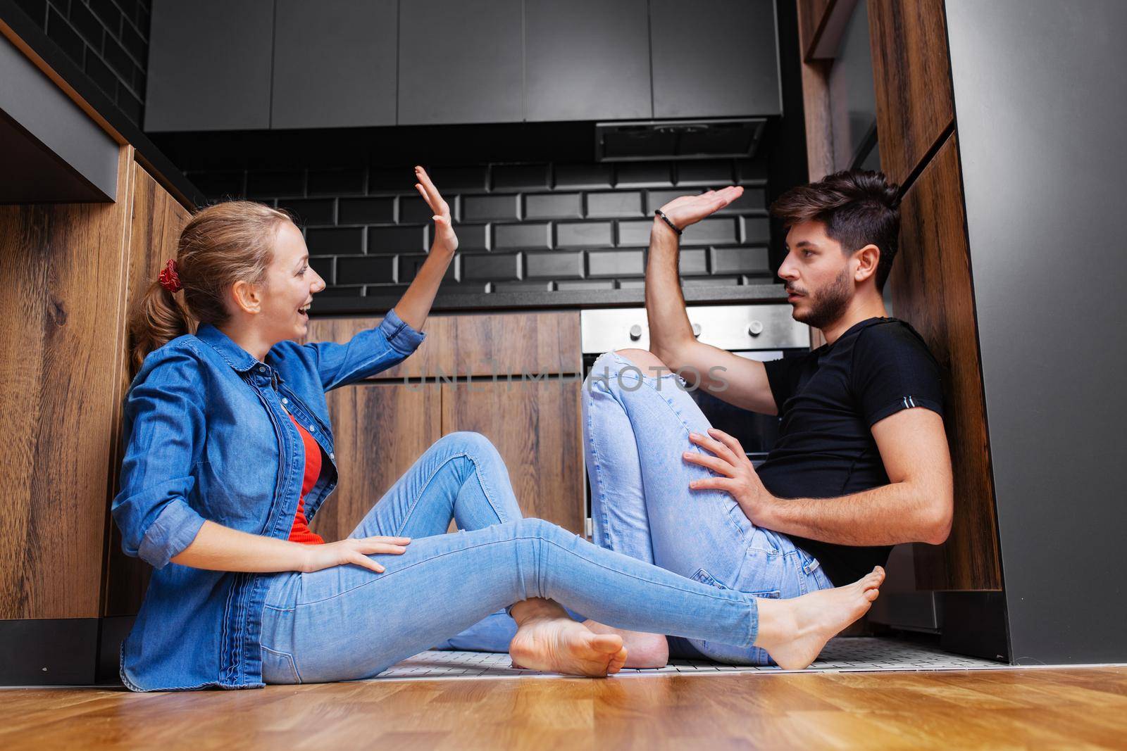 couple giving high five sitting on the floor of a modern kitchen by kokimk