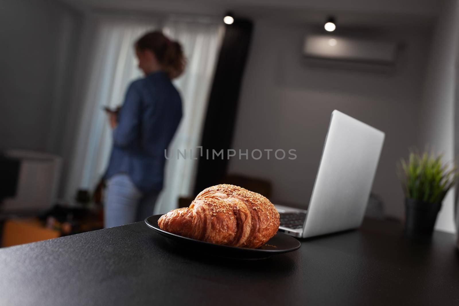 Croissant and laptop on a table in the living room. Out of focus girl in the background