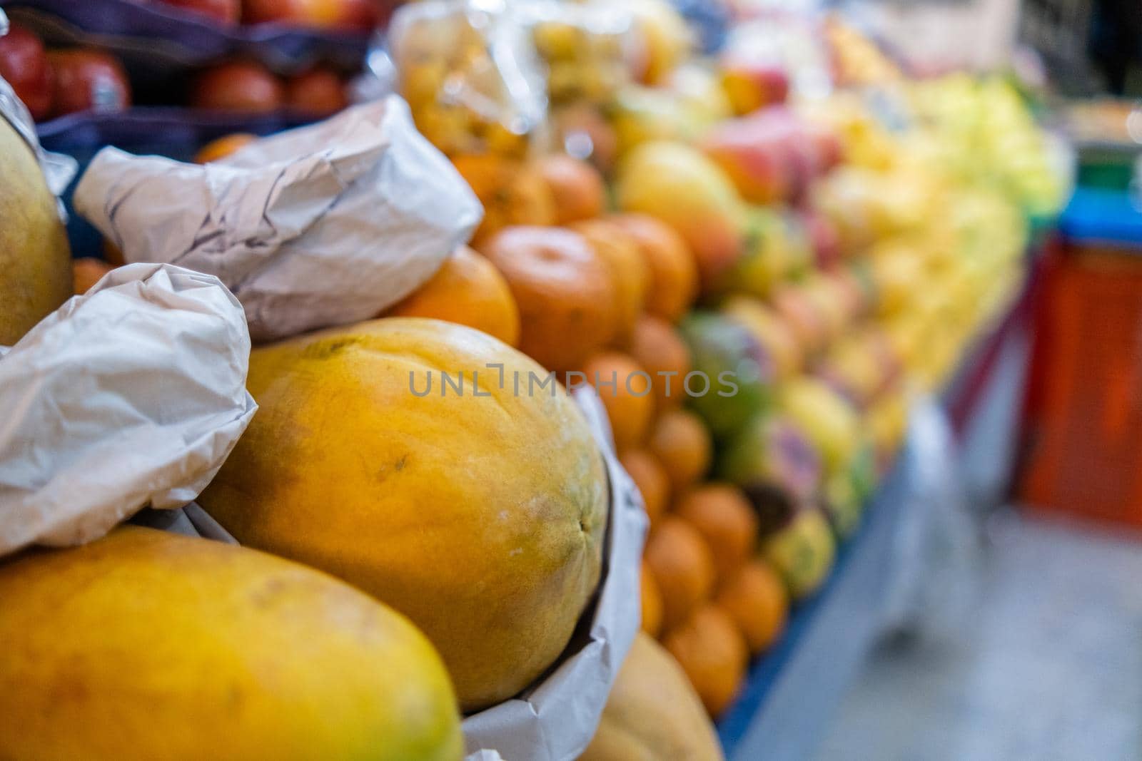 Colorful fruit stand with fresh papayas, tangerines, apples, mangoes, and more. Close-up of juicy-looking fruit for sale on stall inside classic Mexican market with blurry background. Healthy food