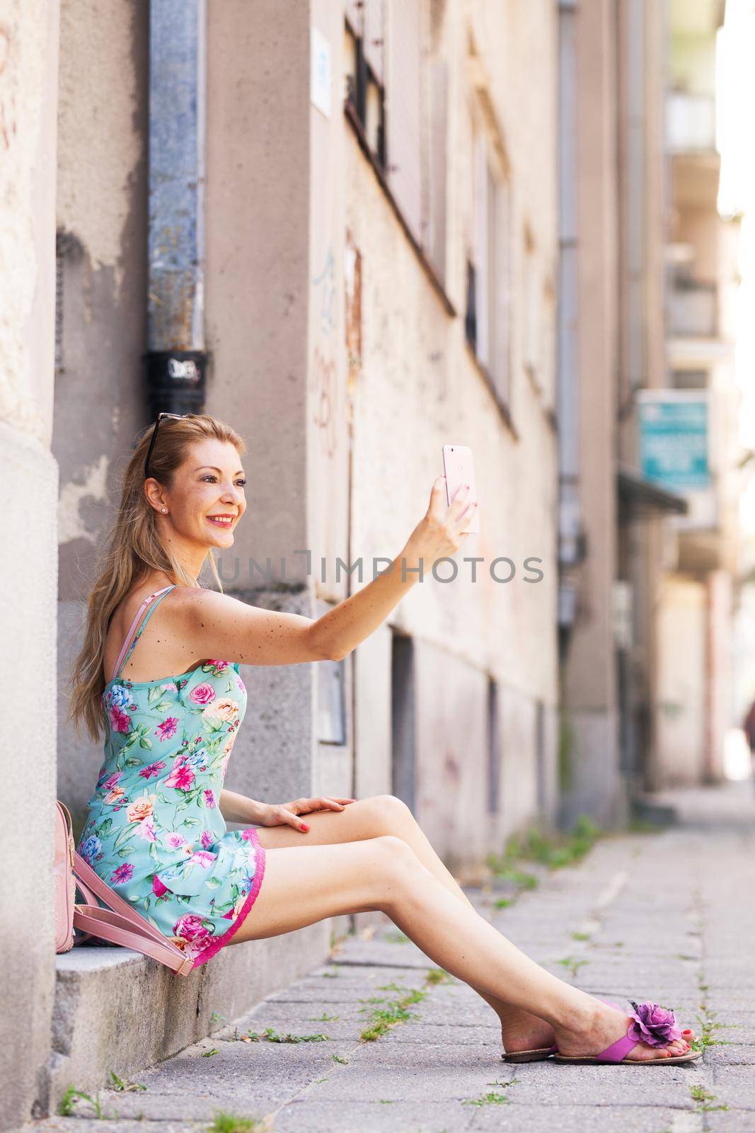 girl sitting on the sidewalk taking selfie photo with her phone