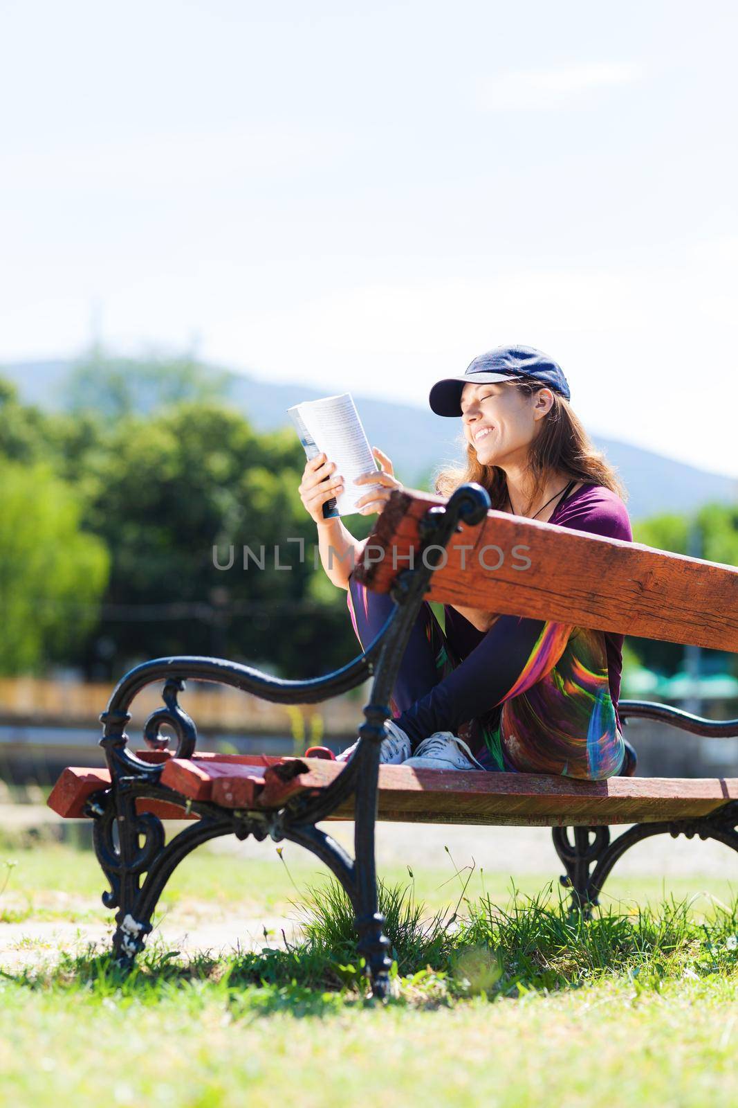 brunette girl with a cap, reading a book sitting on a bench
