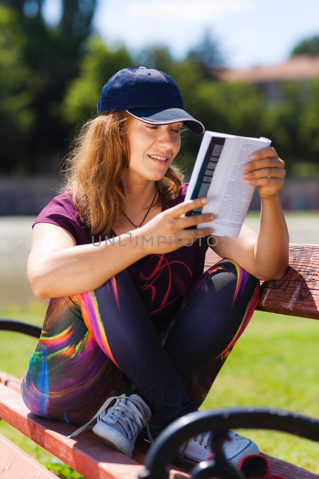 brunette girl with a cap, reading a book sitting on a bench