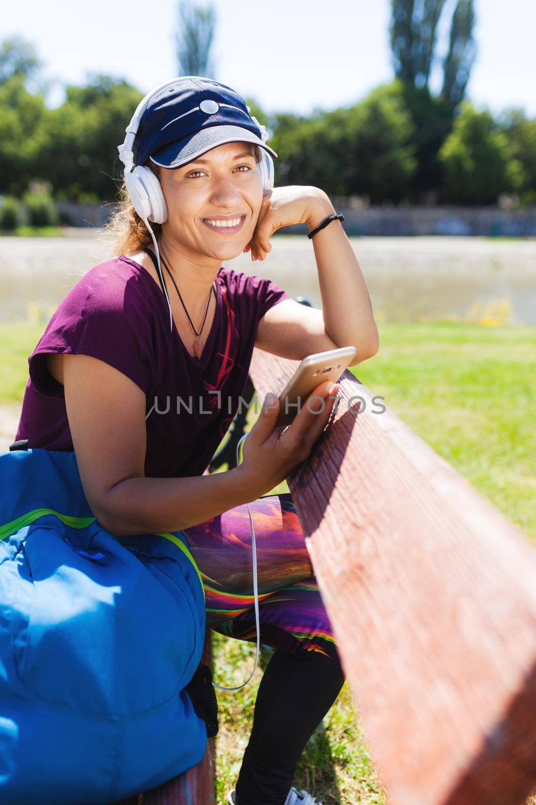 brunette girl with headphones and smartphone listening to music while sitting on a bench