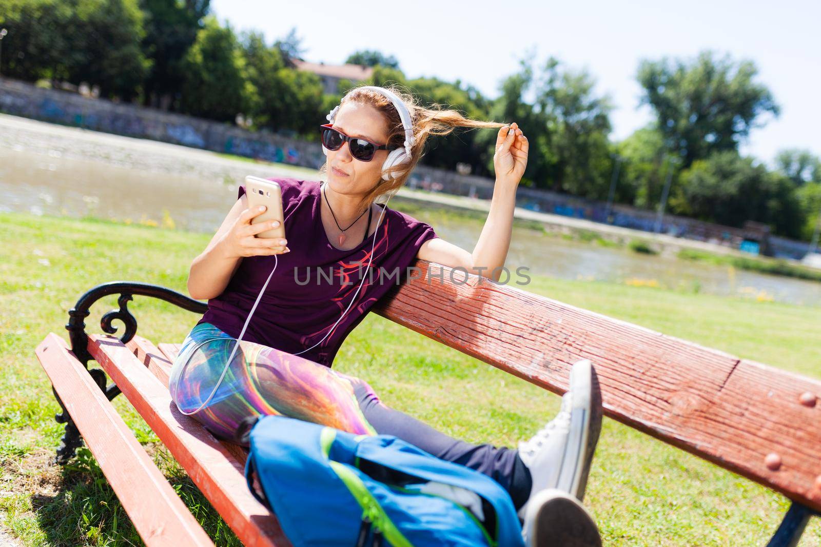 brunette girl with headphones, taking a selfie while sitting on a bench by kokimk