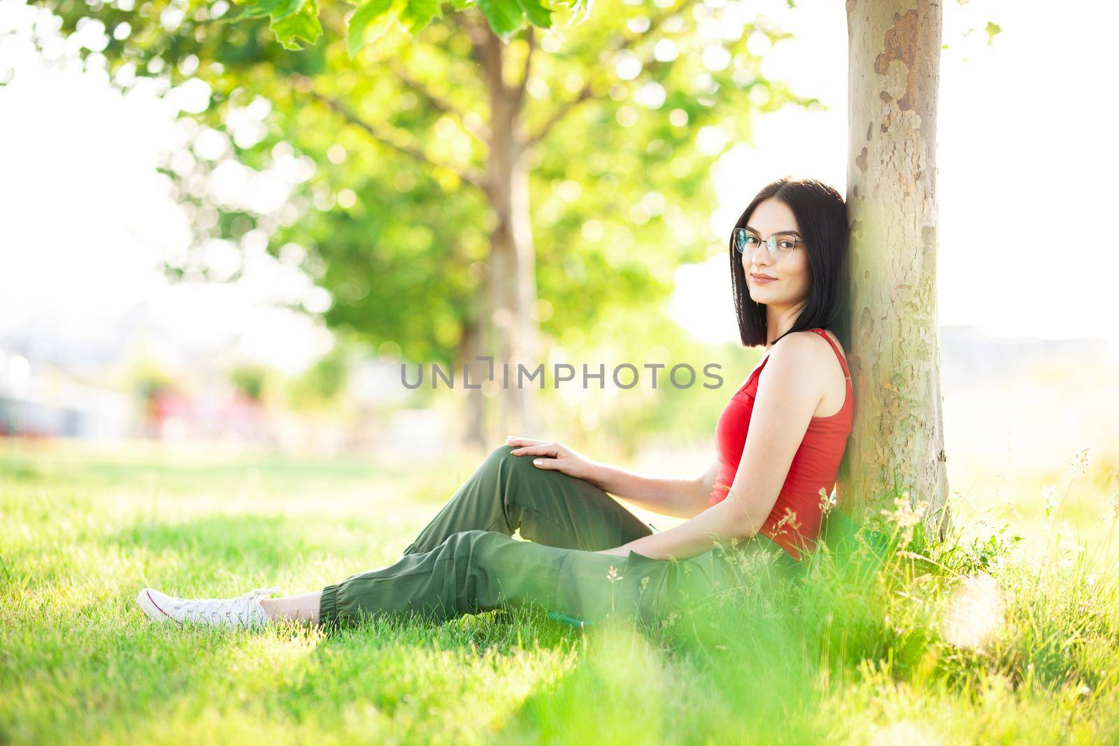 girl with dark brown hair and glasses sitting under a tree