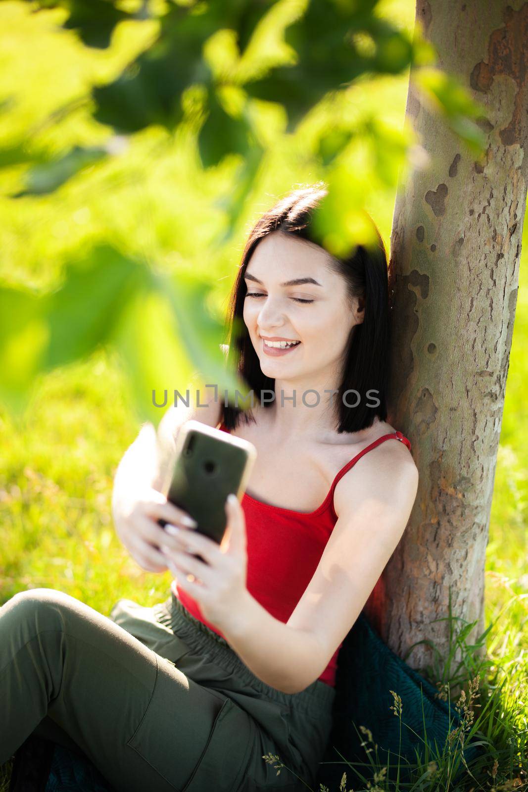 girl with dark brown hair using smartphone taking selfy under a tree