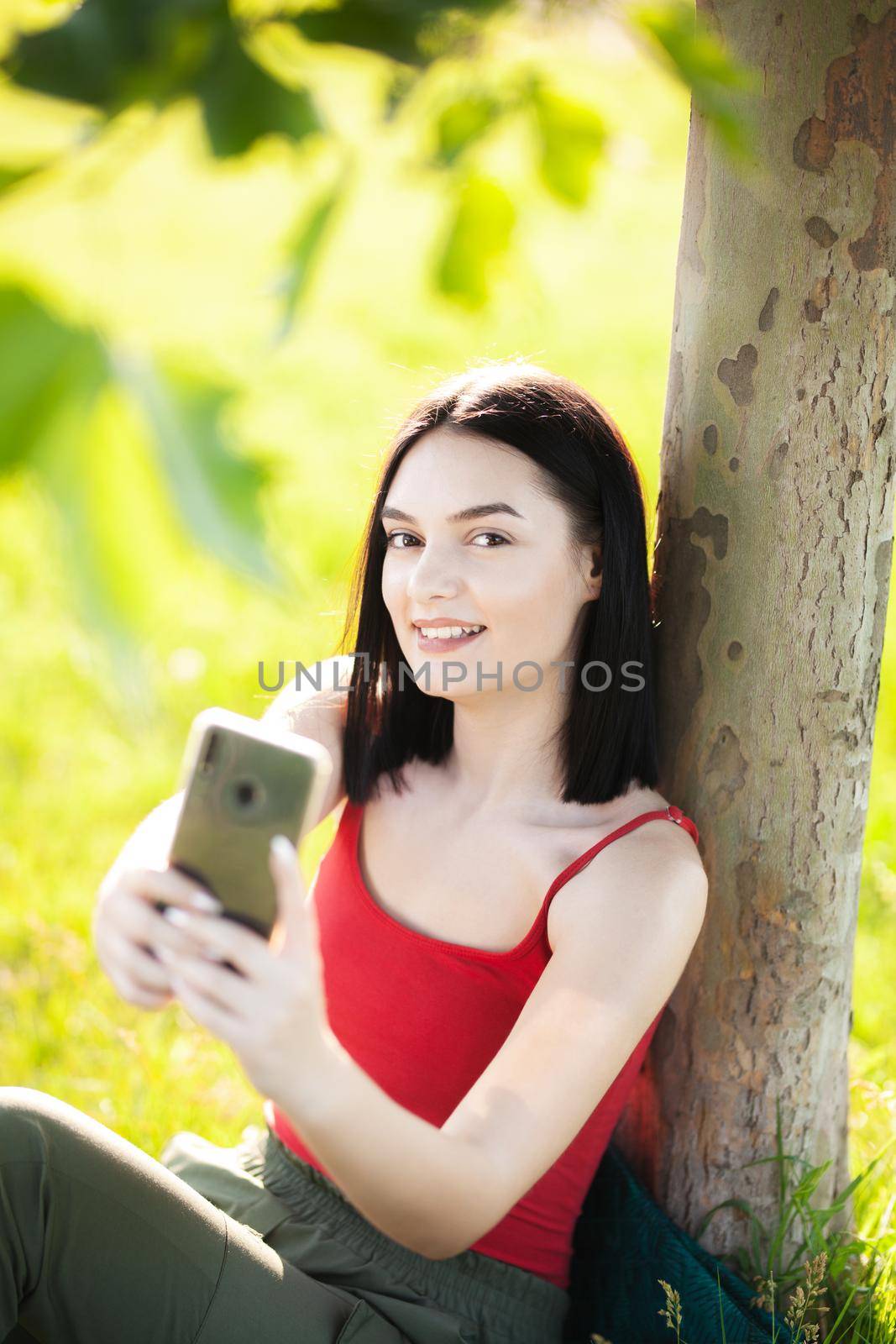 girl with dark brown hair using smartphone taking selfy under a tree