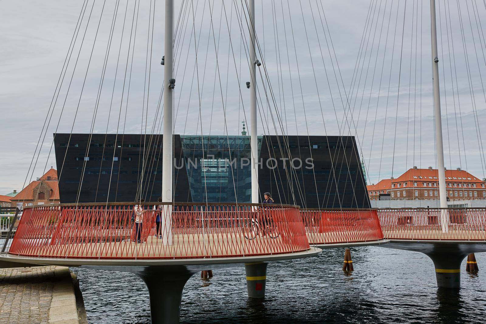 COPENHAGEN, DENMARK - JUNE 28, 2017: People crossing the bridge and The Black Diamond in the background. The Copenhagen Royal Library is the national library of Denmark in Copenhagen.