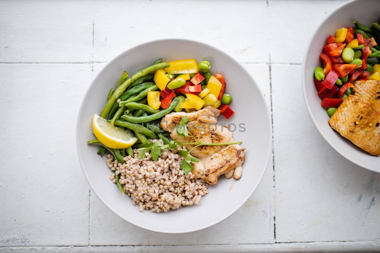 Top view of chicken and buckwheat dish with green beans, broad beans, tomato, and pepper slices. Nutritious dishes with vegetables and meat on white plates. Healthy balanced diet