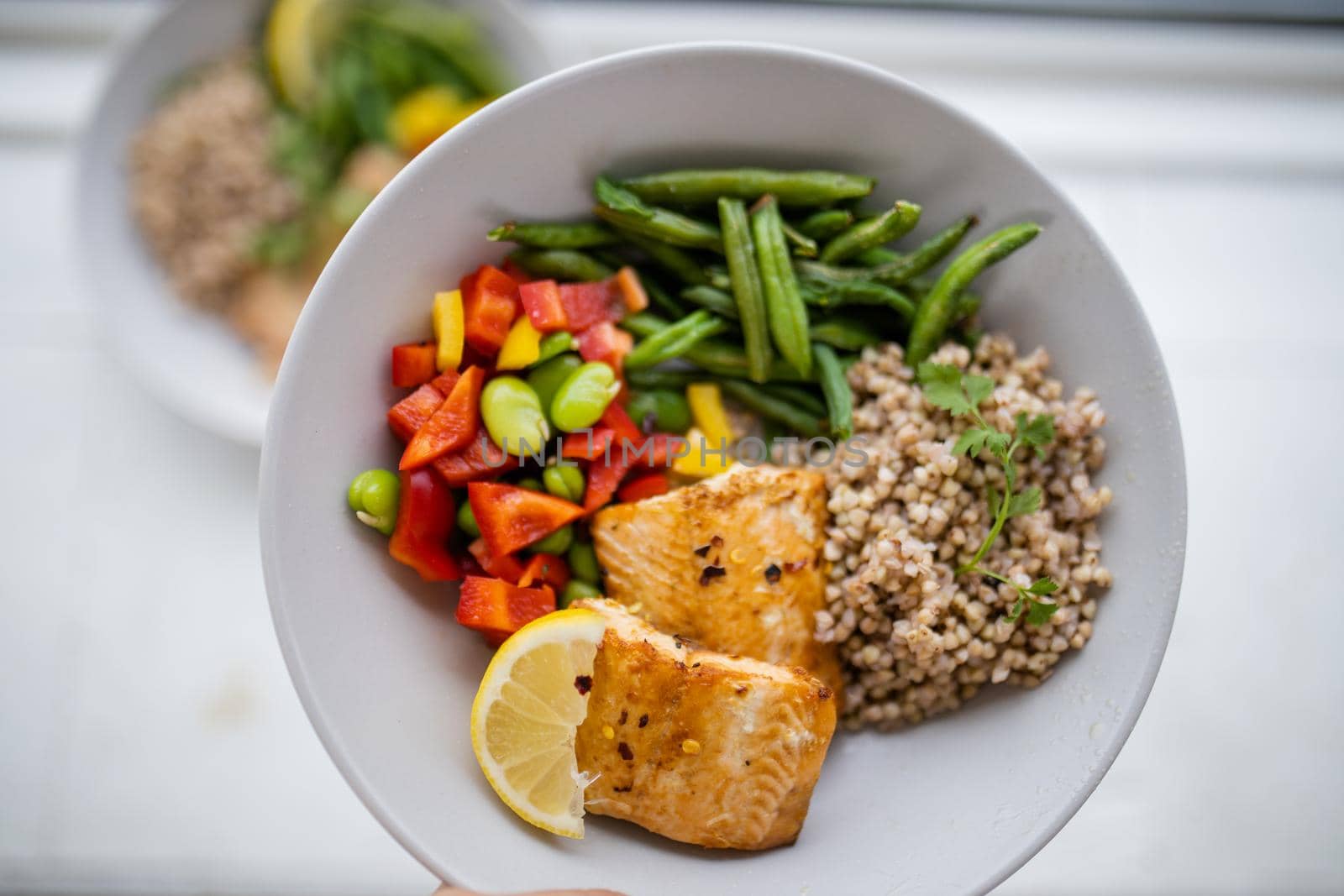 Top view of salmon and buckwheat dish with green beans, broad beans, and tomato slices. Nutritious dish with vegetables and fish on white plate. Healthy balanced diet