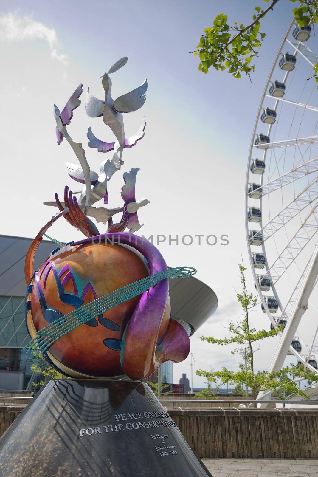 LIVERPOOL, ENGLAND, UK - JUNE 07, 2017: Peace on earth sculpture in honour of John Lennon with the Echo wheel of Liverpool to the rear at Keel Wharf, Liverpool, Merseyside, England, UK