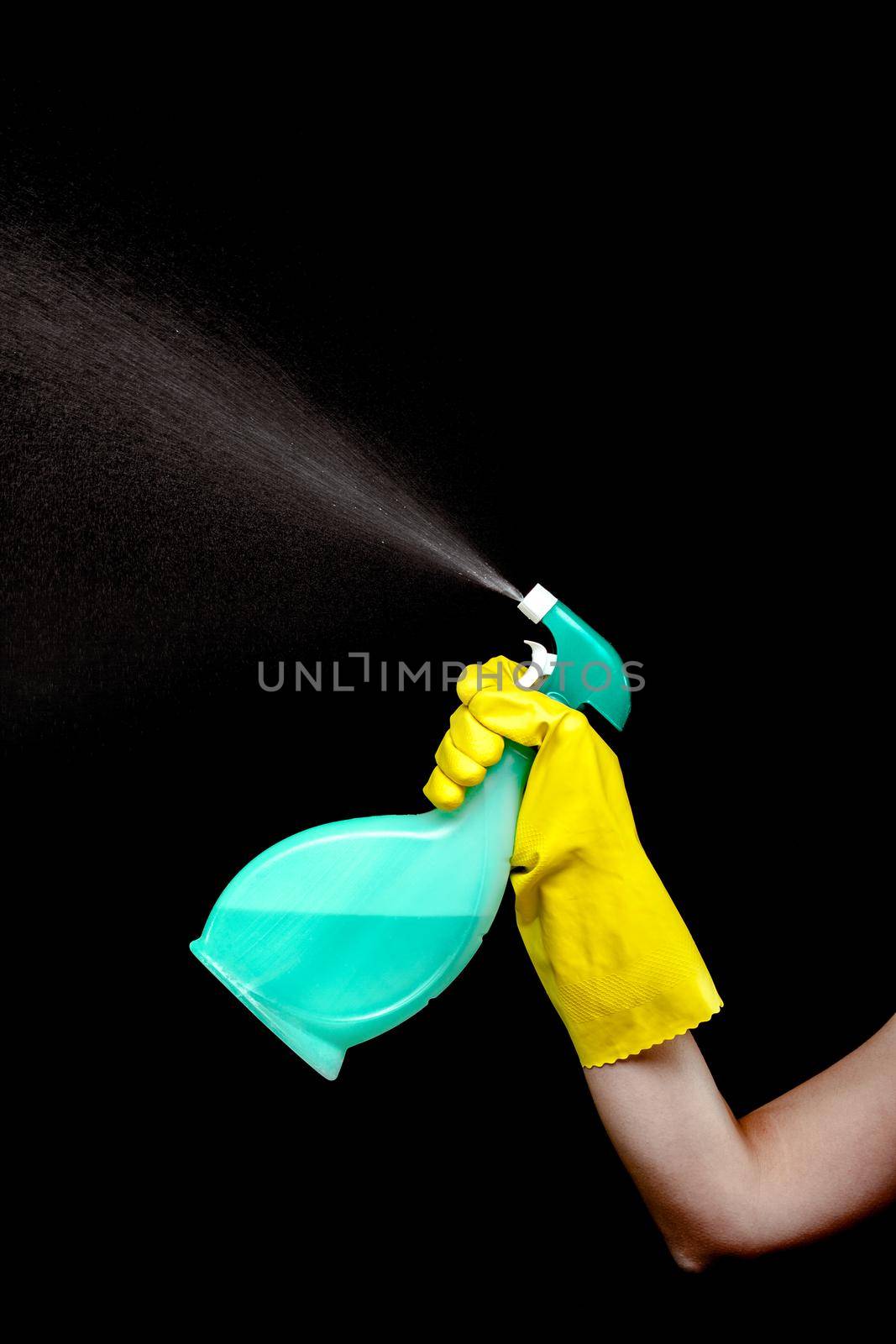 hand in yellow glove spraying liquid cleaning detergent in the air against black background