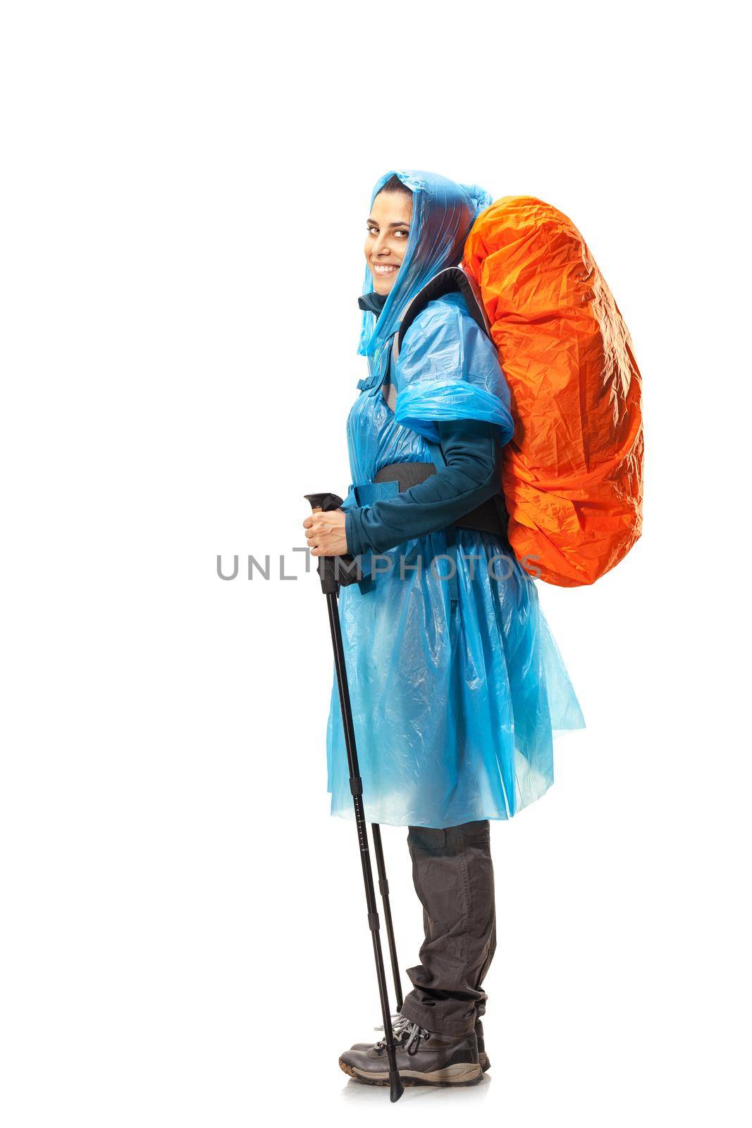 girl with hiking equipment and large backpack, wearing blue raincoat, posing in studio isolated on white.