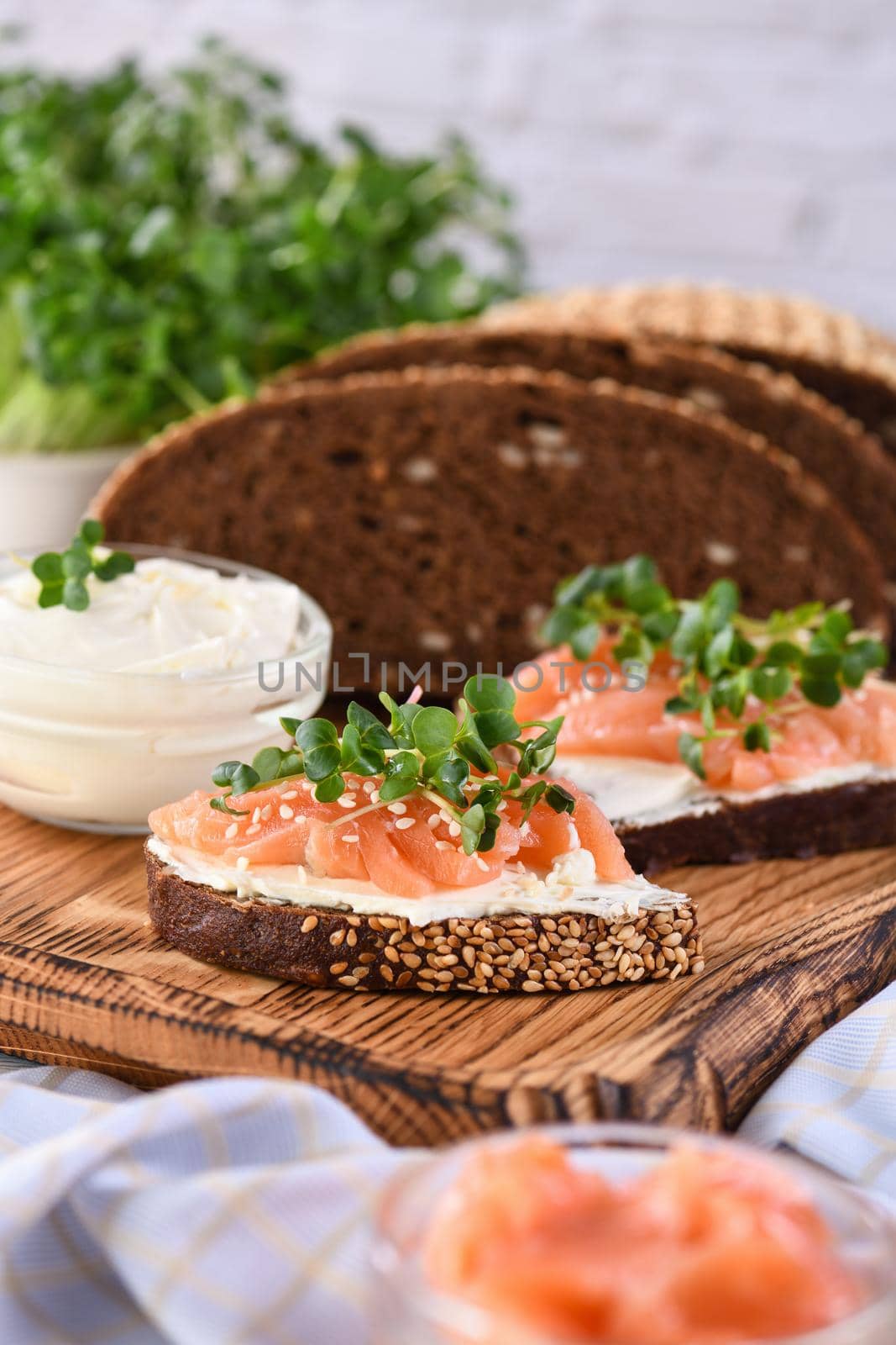 Open sandwich with cheese cream on a slice of rye bread with cereals, slices of marinated salmon, and radish sprouts.