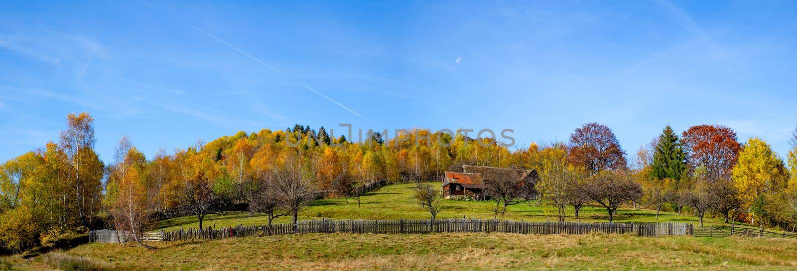 a cottage surrounded by a fence in an atmosphere of autumn with moon, Fantanele village, Sibiu county, Romania by Roberto