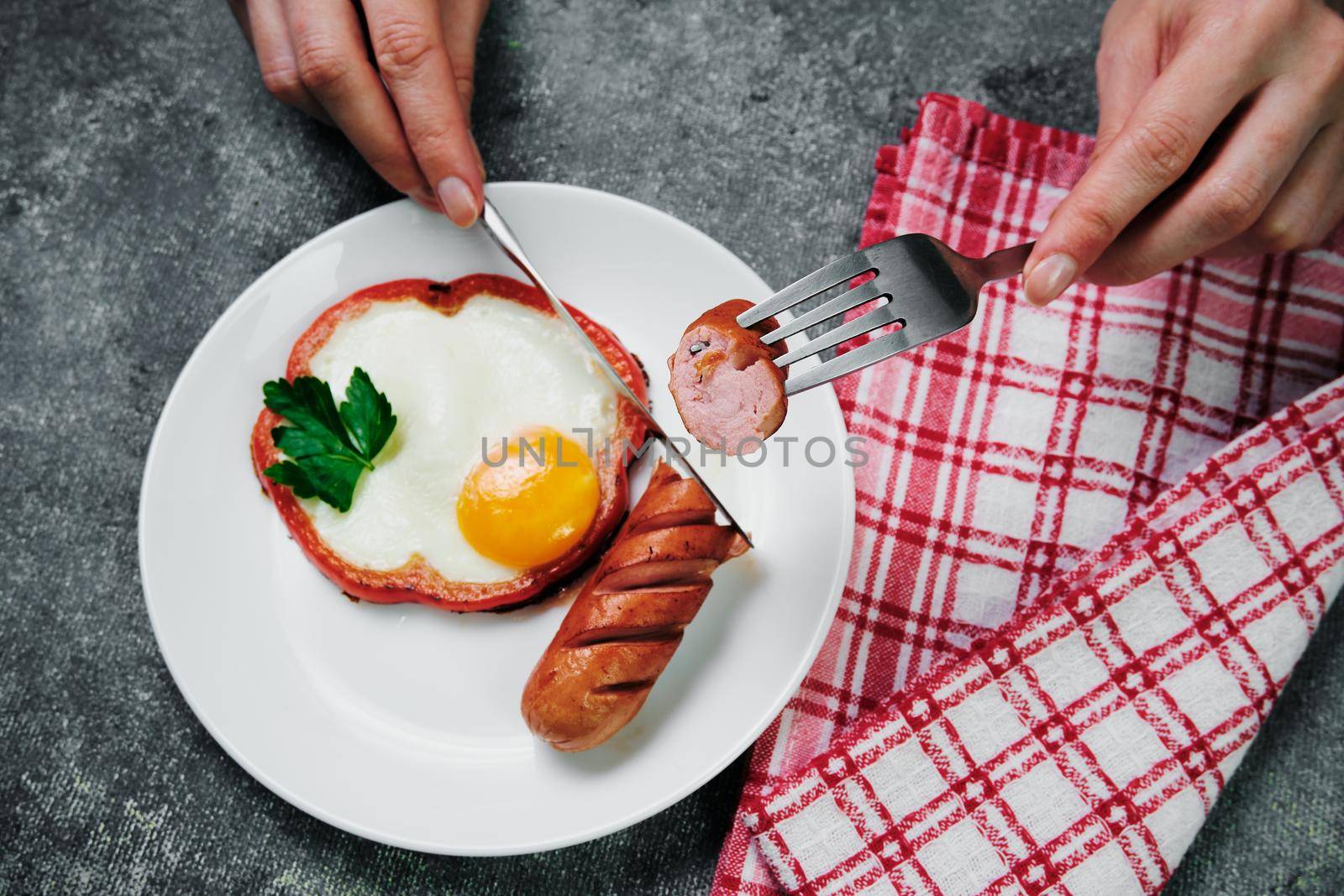 fried egg, red pepper, sausage, towel and cutlery on a dark table