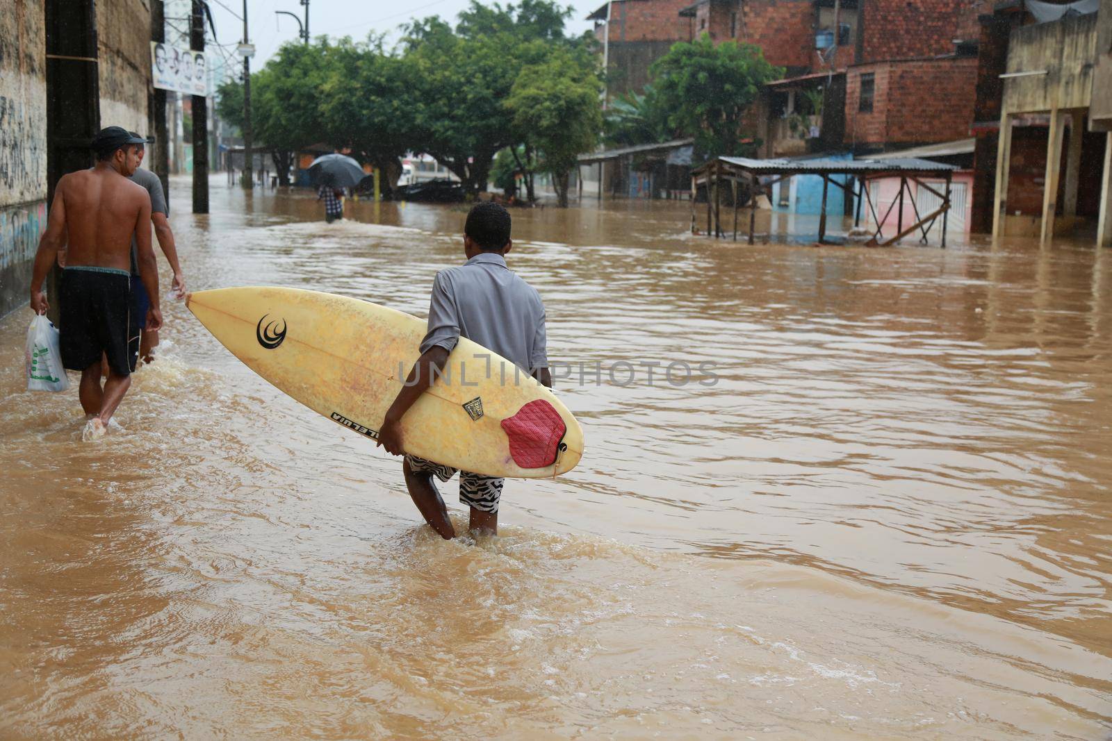 salvador, bahia / brazil - April 27, 2015: Young man is seen with surfboard in flooded area during rainy season community of Bate-faxo in the city of Salvador.