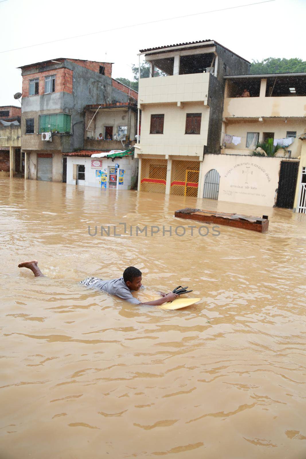 salvador, bahia / brazil - April 27, 2015: Young man is seen with surfboard in flooded area during rainy season community of Bate-faxo in the city of Salvador.