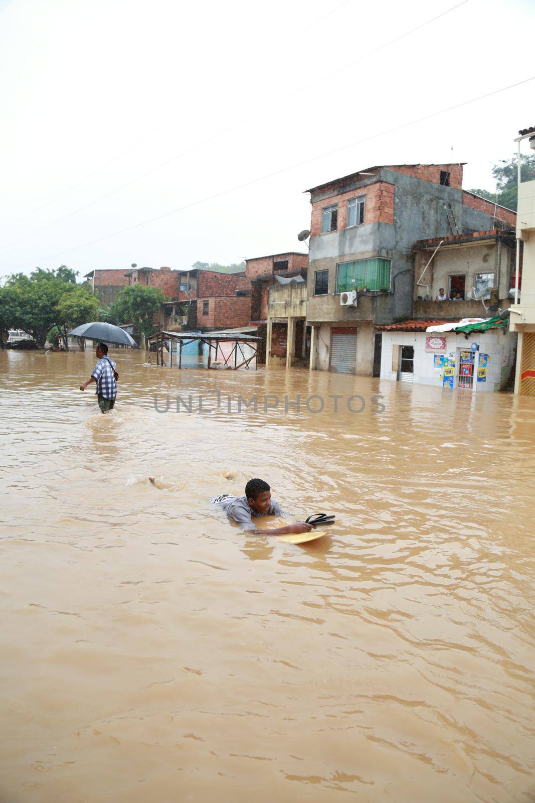 salvador, bahia / brazil - April 27, 2015: Young man is seen with surfboard in flooded area during rainy season community of Bate-faxo in the city of Salvador.