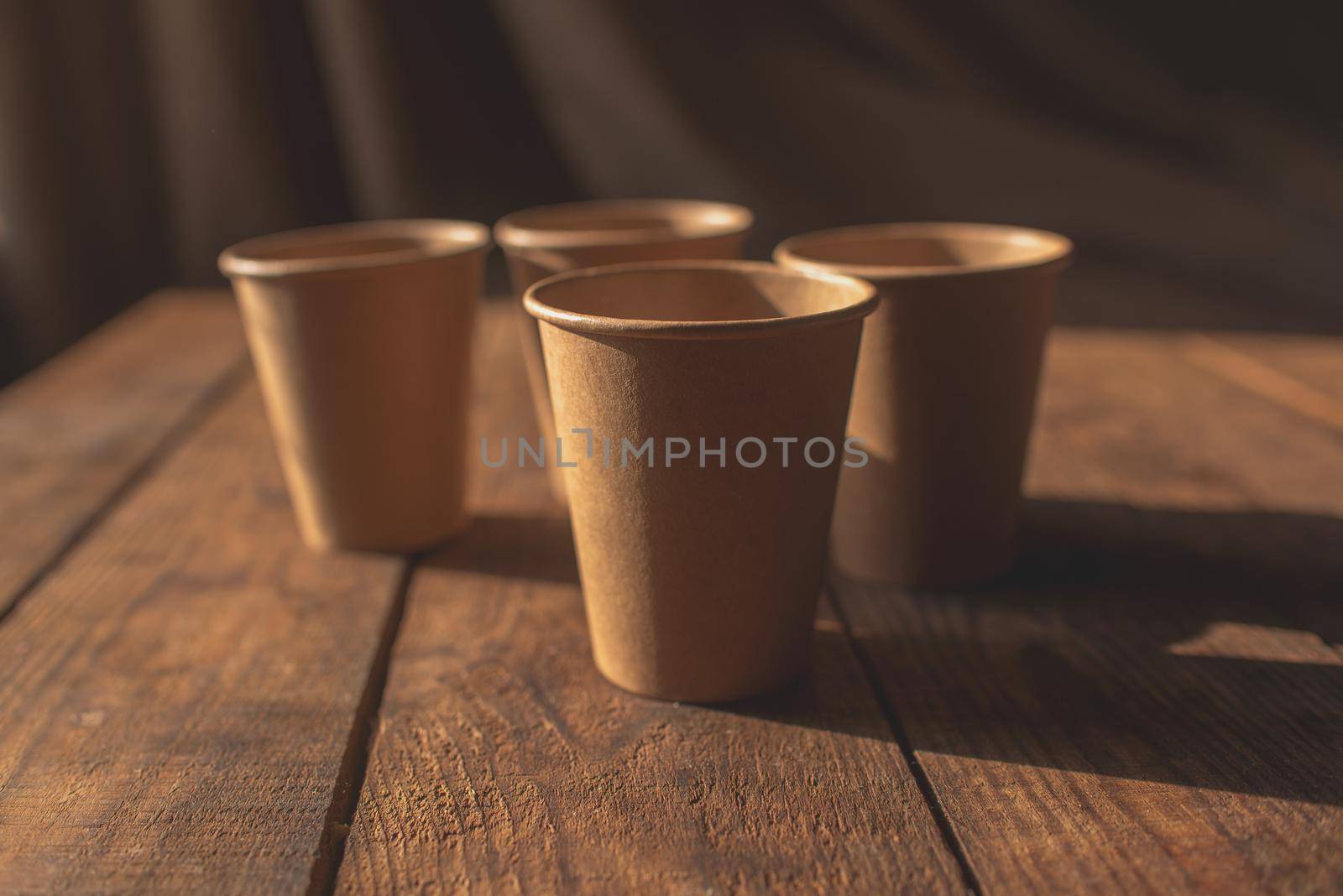 Disposable dark brown kraft paper cups stand on wooden table against brown background