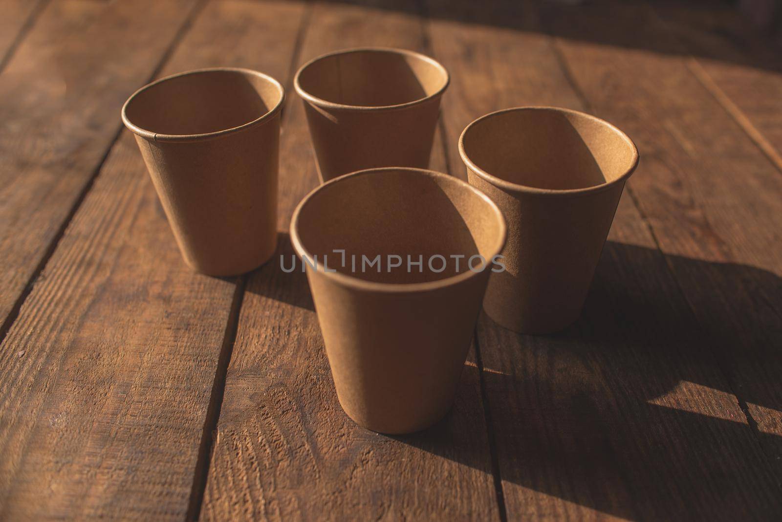 Disposable dark brown kraft paper cups stand on wooden table against brown background
