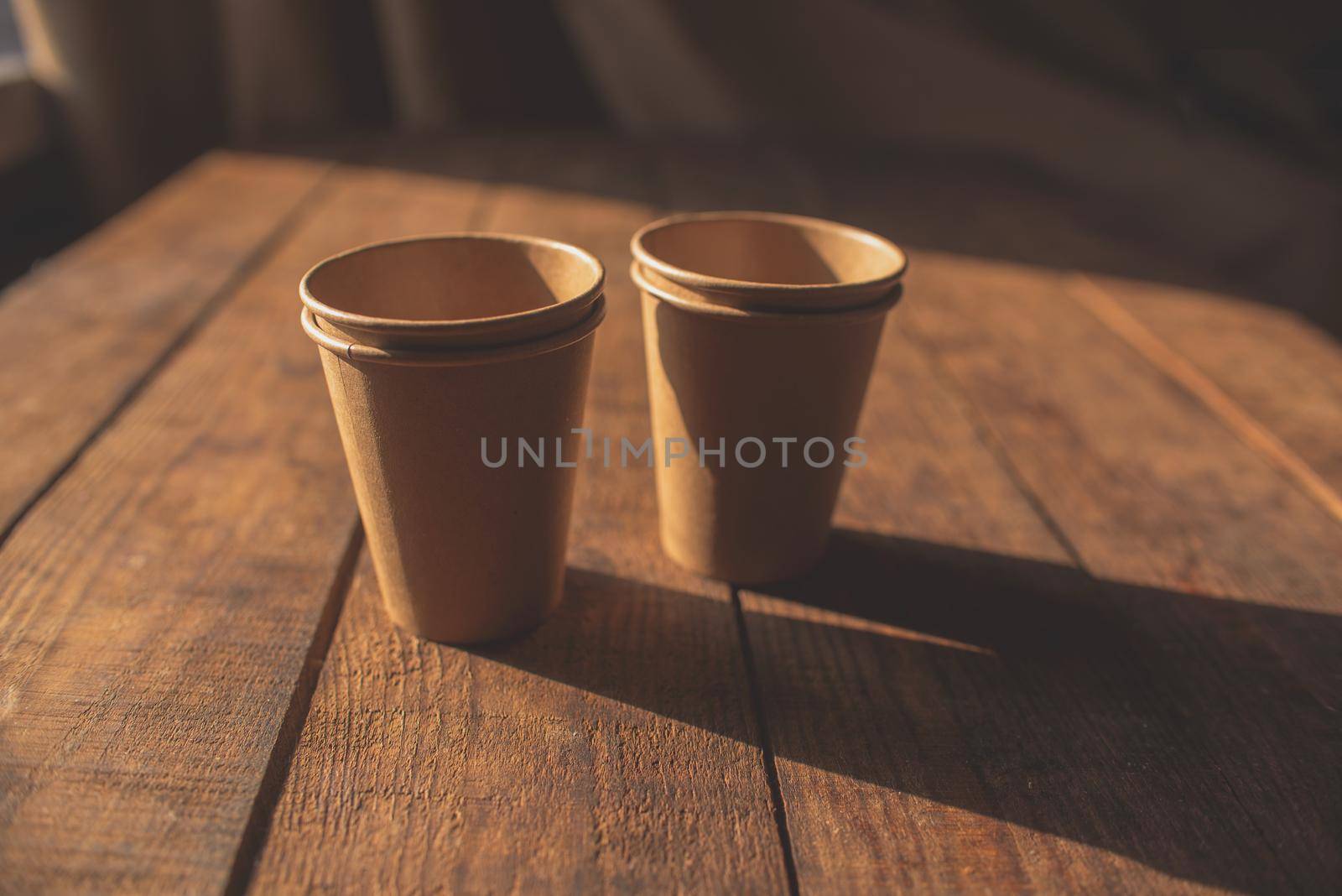 Disposable dark brown kraft paper cups stand on wooden table against brown background