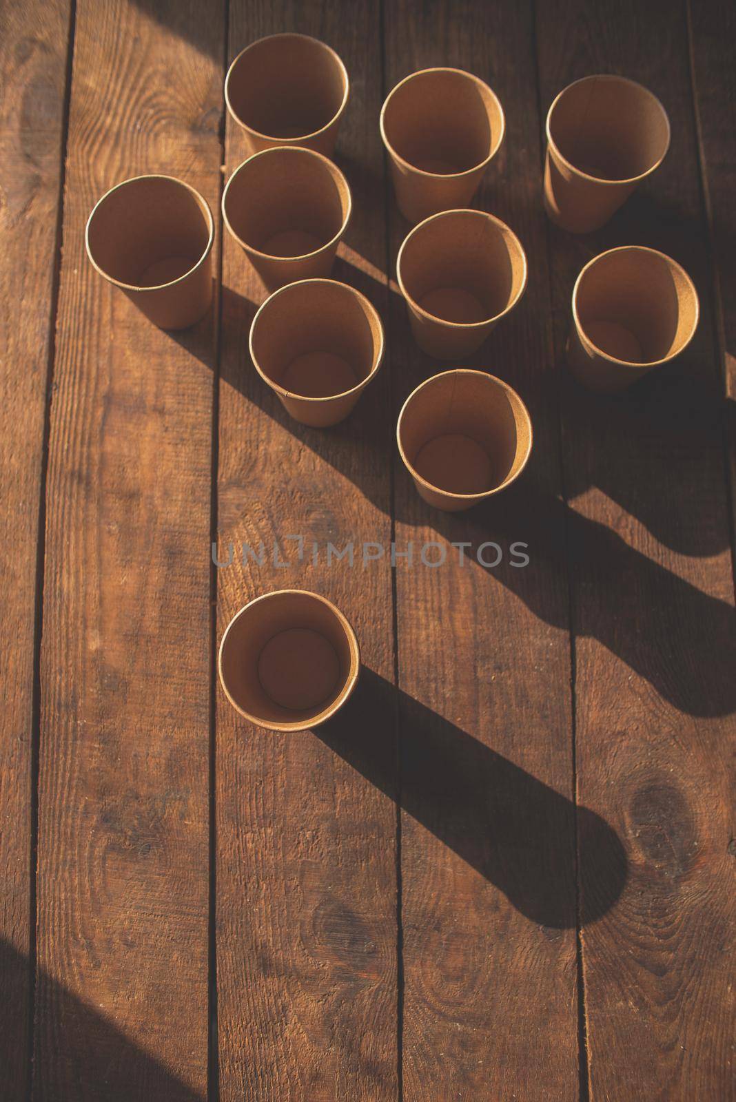 Disposable dark brown kraft paper cups stand on wooden table against brown background