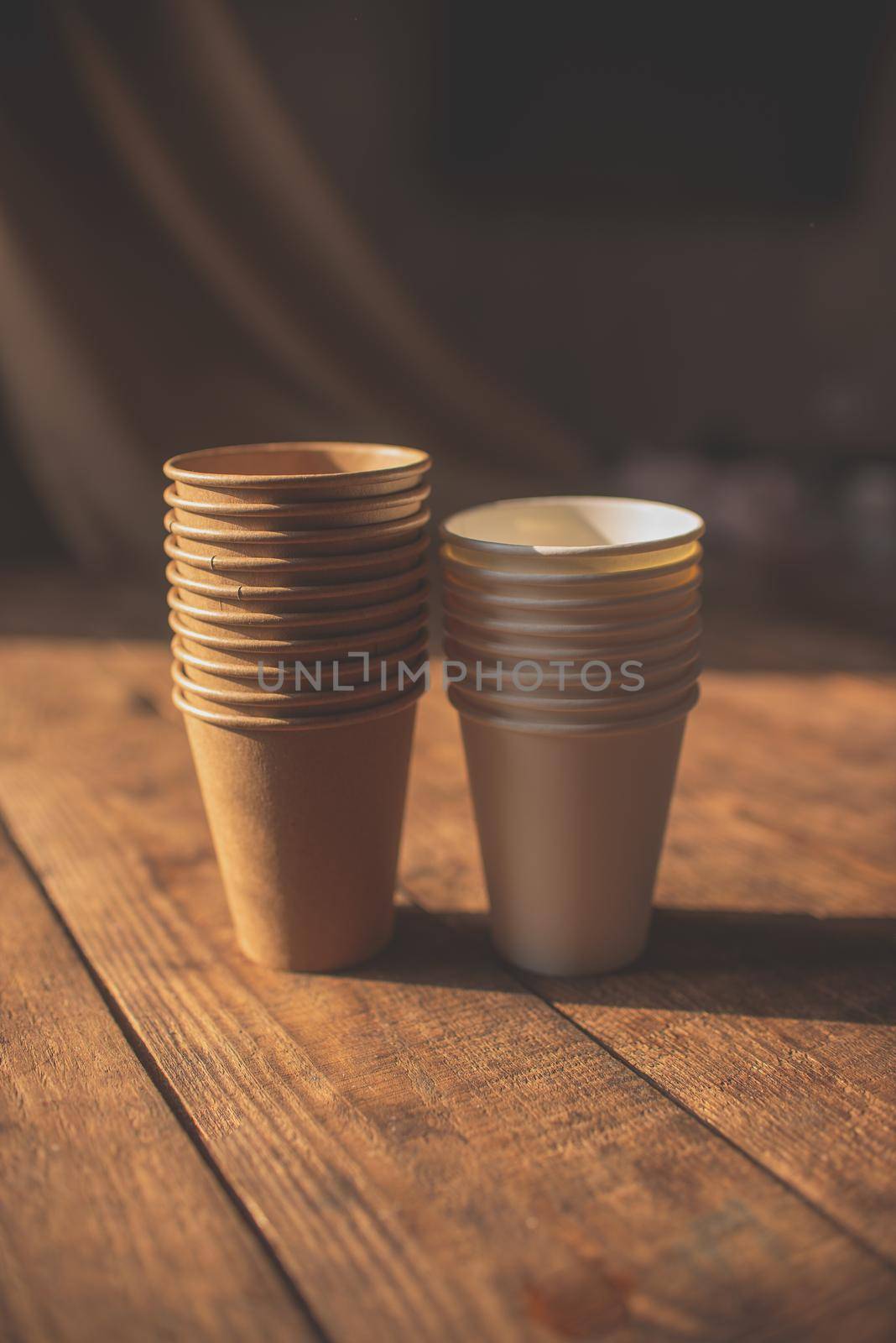 disposable cups made of dark brown paper and white cups stand on wooden table against brown background