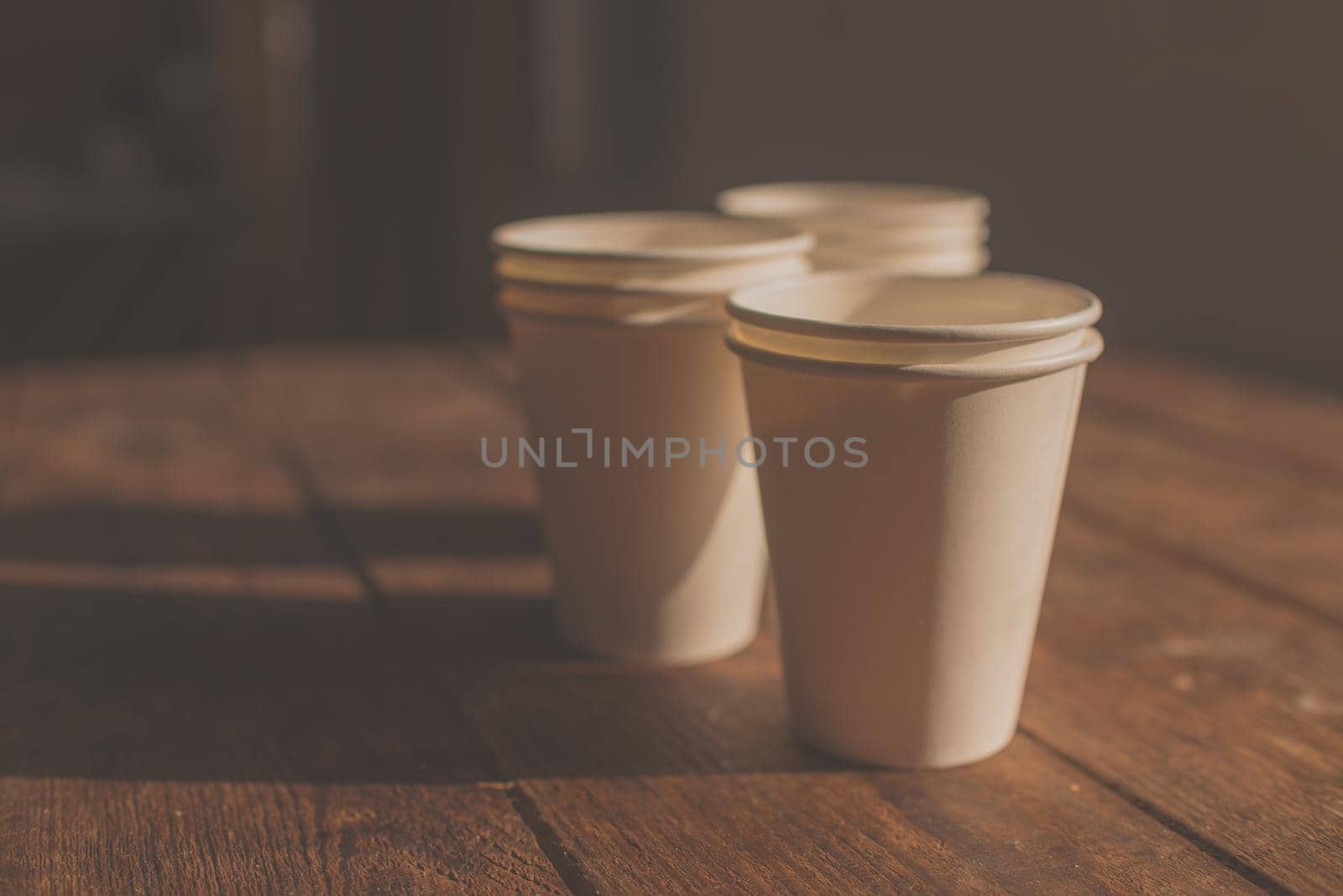 disposable white cardboard cups stand on a wooden table on a brown background